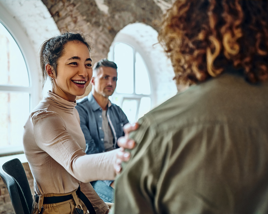 Eine Frau lacht in einem Raum mit einem Mann im Hintergrund.