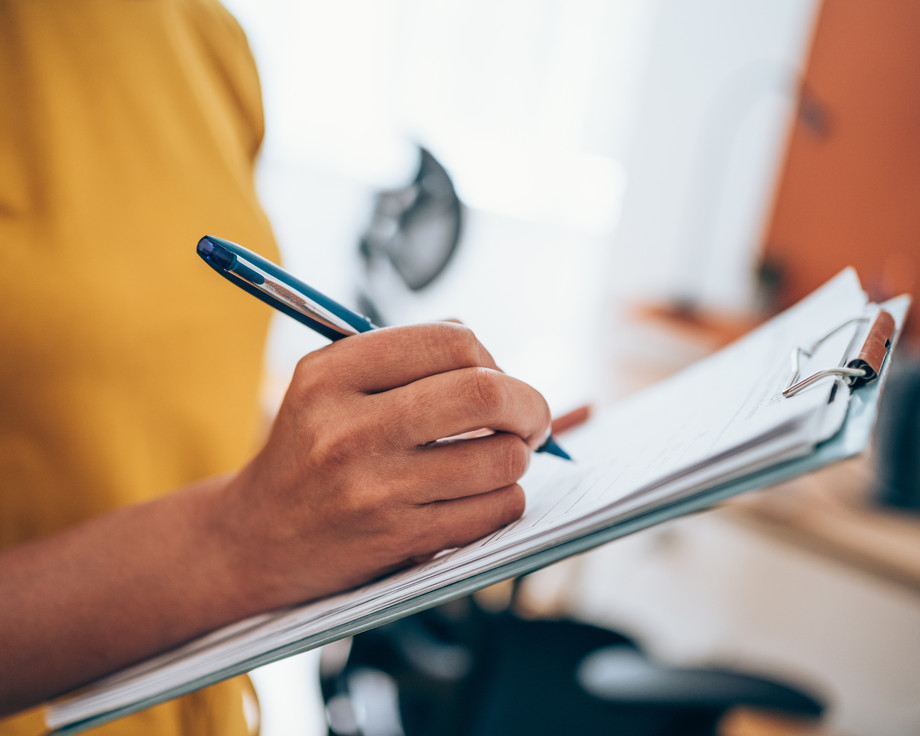 Person schreibt auf einem Klemmbrett mit einem Stift.