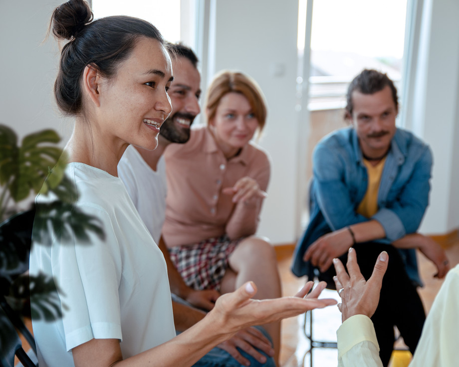 Eine Frau hält eine Flasche und sprüht sich Desinfektionsmittel auf die Hände, während drei Personen im Hintergrund zusehen.