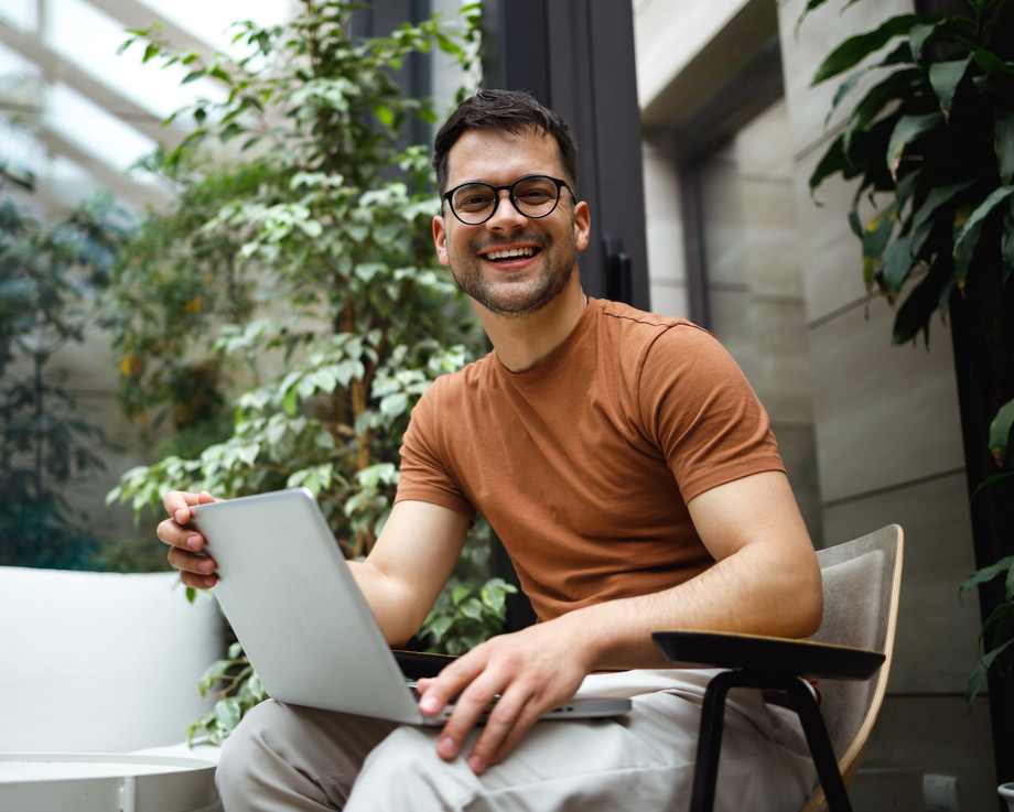 Ein Mann sitzt an einem Tisch und arbeitet an einem Laptop, umgeben von Topfpflanzen.
