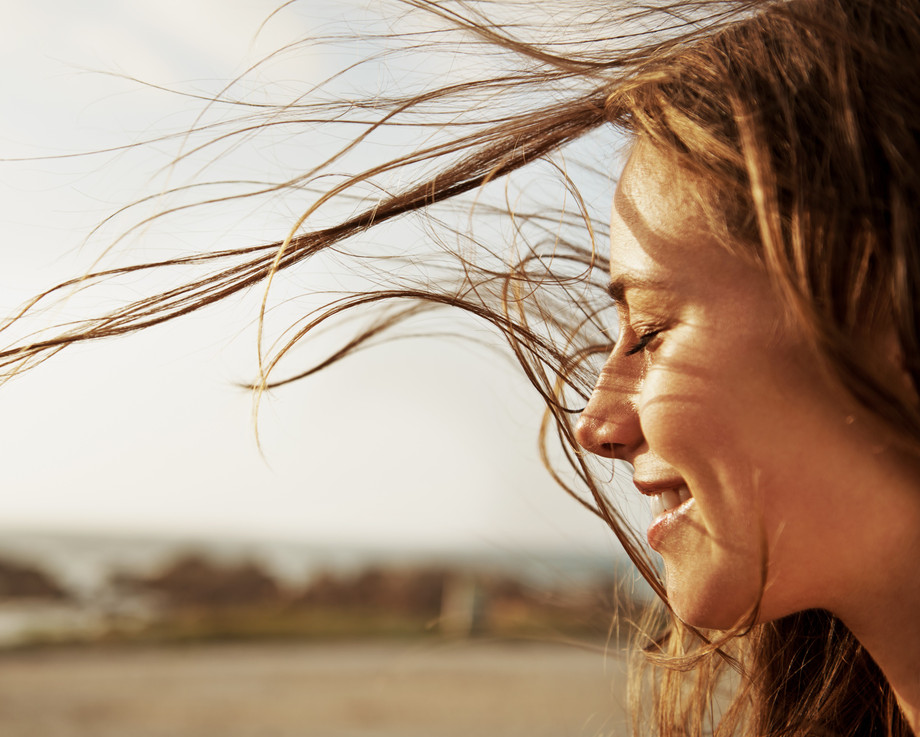 Eine Person mit wehendem Haar steht am Strand.